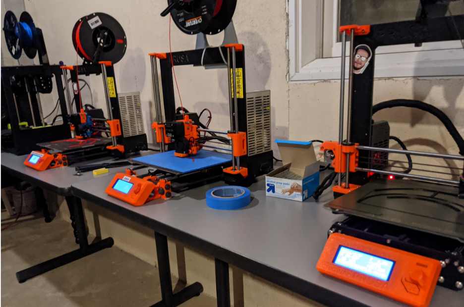 3D Printers lined up on fold out tables in a students unfinished basement. 